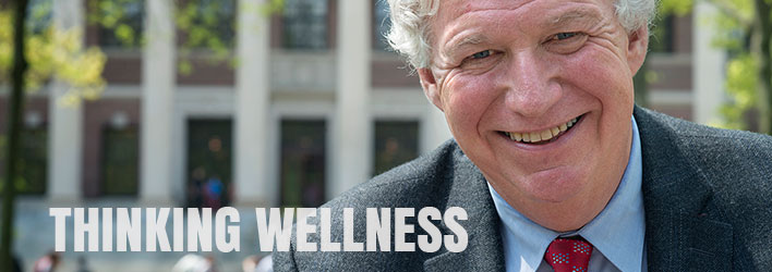 Photo of a smiling man wearing a suit and tie with the words THINKING WELLNESS below.