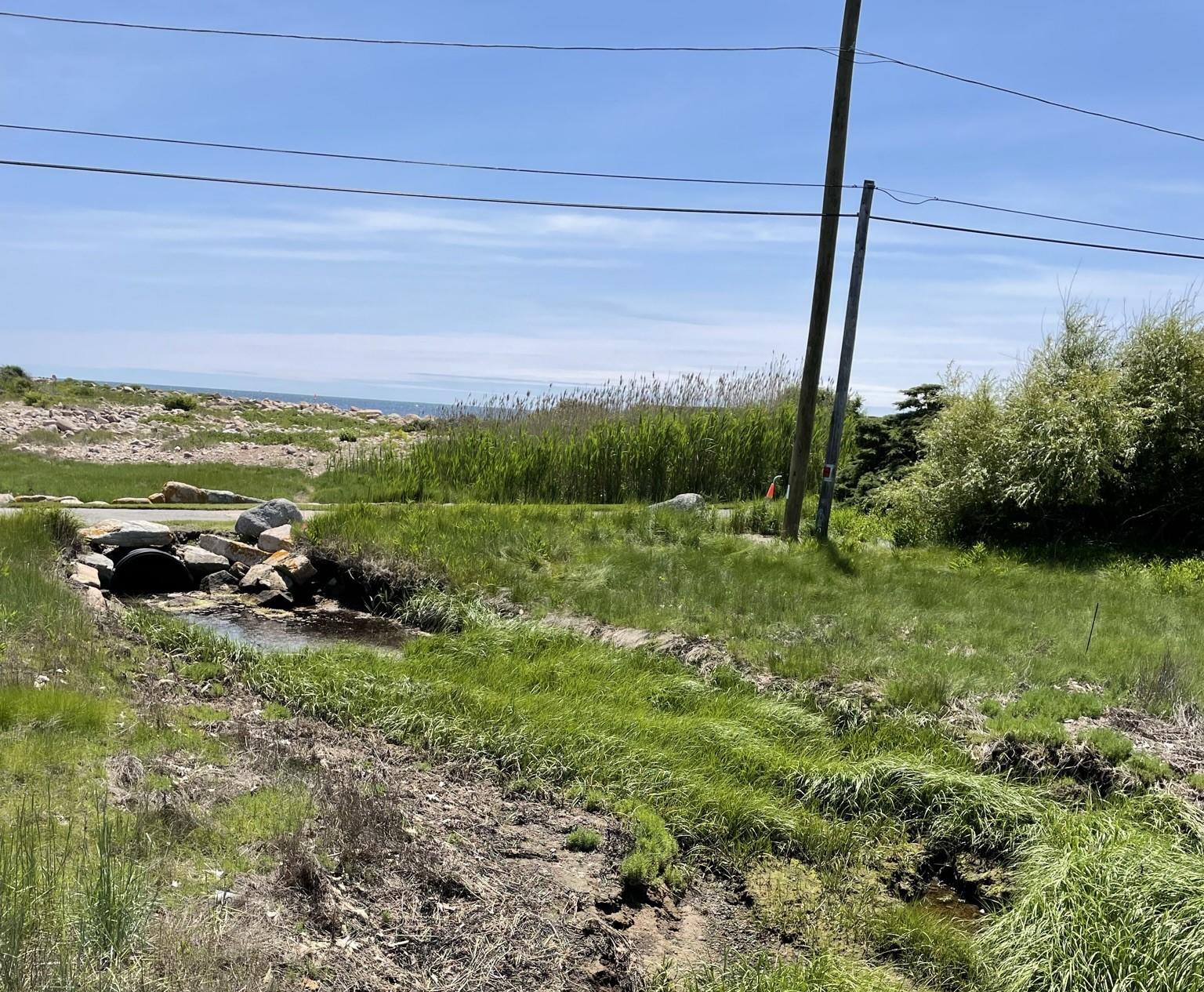 Culvert in grassy area with ocean in background.