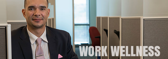 Photo of man wearing a suit and tie sitting in an office environment and the words WORKING WELLNESS underneath.