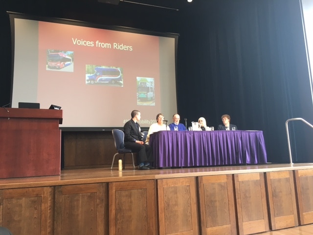 Four panelists and one facilitator on a stage with a backdrop that says "Voices from Riders"