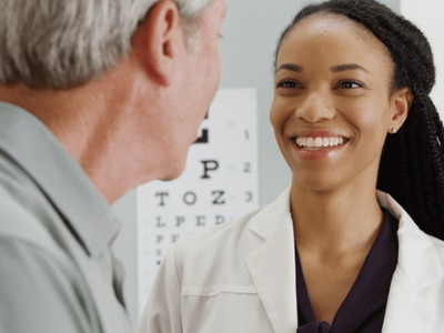 Patient standing with Eye Care Provider in exam room with eye chart in background