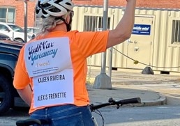 Person on bicycle with "youth vax giveaway" sign
