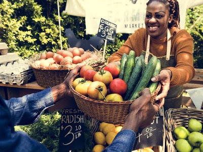 Female Black farmer holding a basket of fresh produce at a farm stand