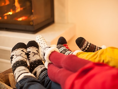 3 people warming their feet by a fireplace