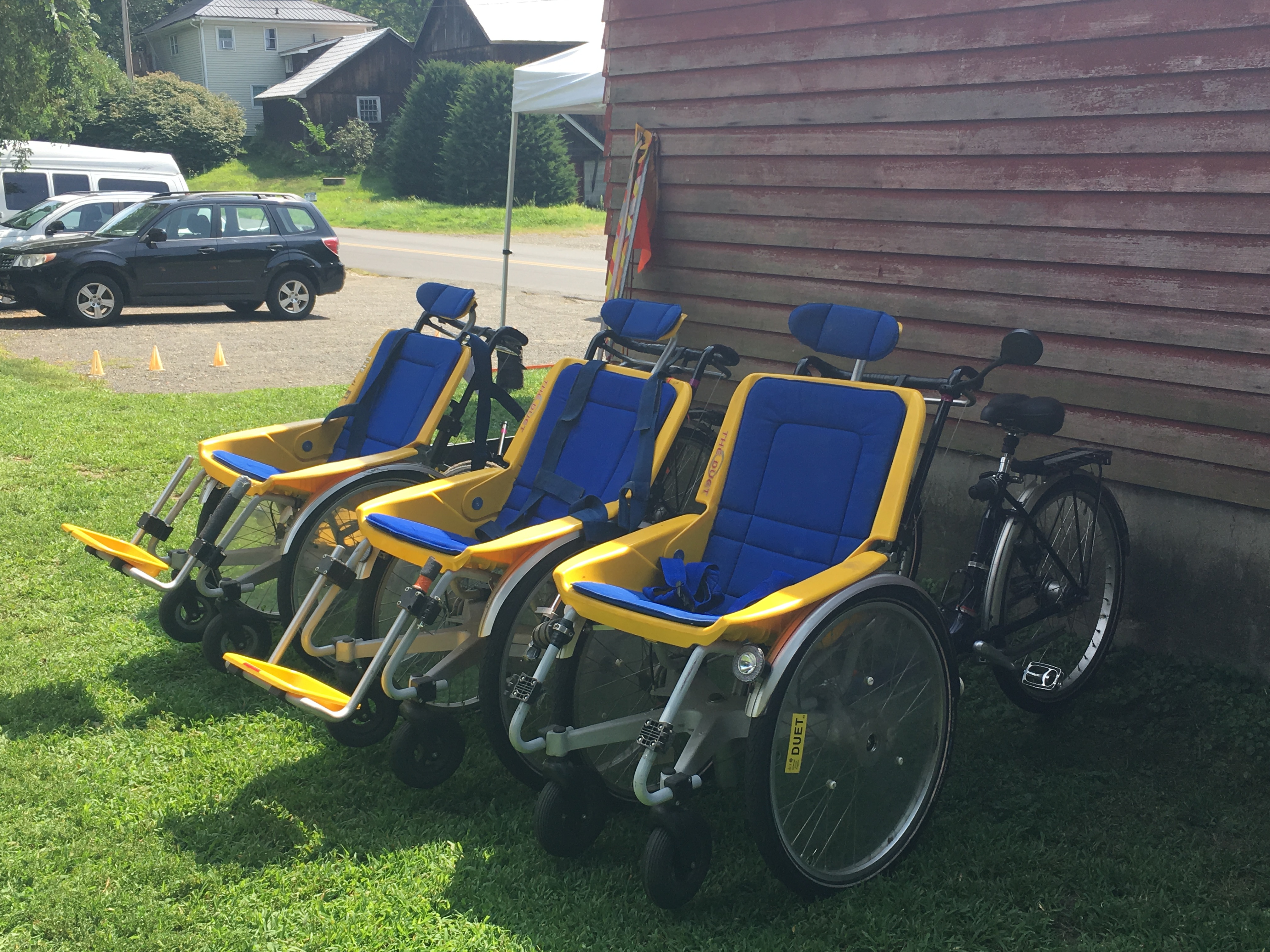 Three Frank Mobility Duet Wheelchair Tandem Bikes lined up next to a brick building