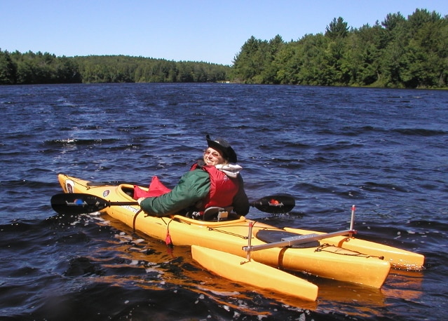 A paddler in a single kayak with outriggers on the back.