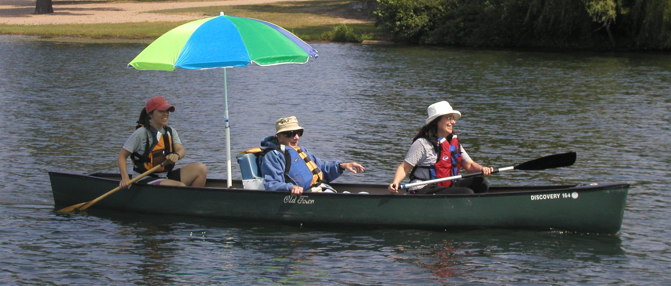 Three paddlers in a canoe. The center paddler is sitting in a padded seat with side support that is placed in the bottom of the canoe.