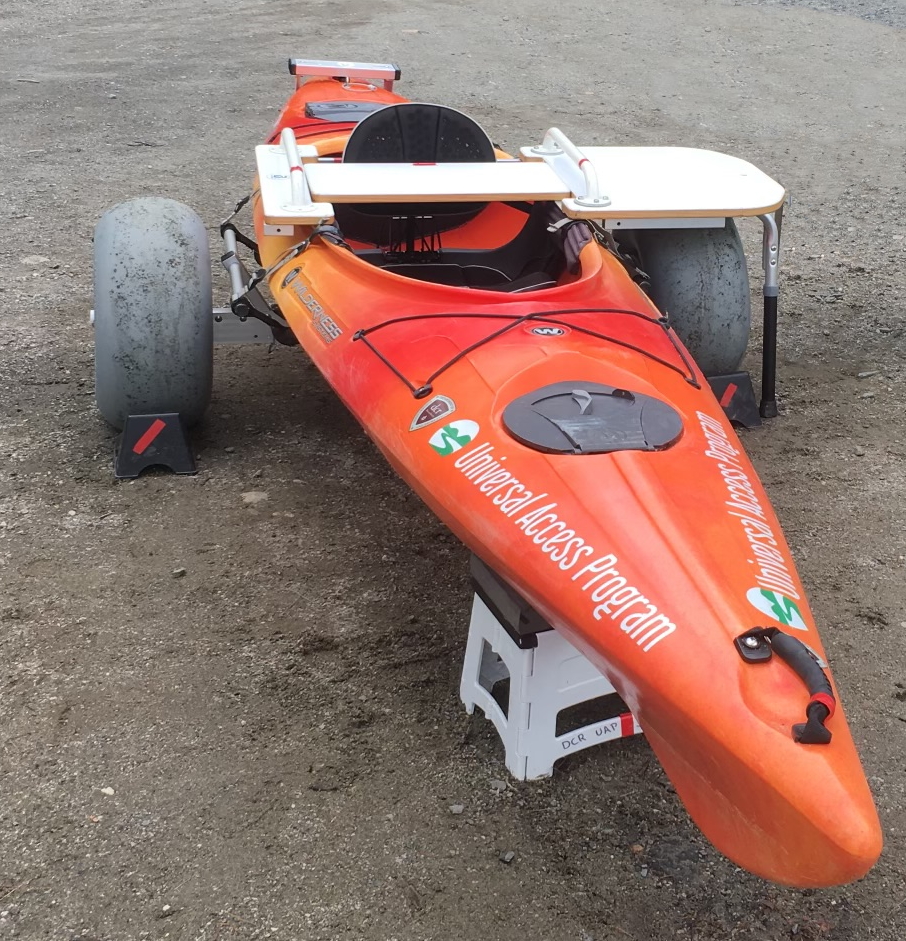 A kayak raised up on large balloon wheels. A white bench straddles the kayak over the seat.