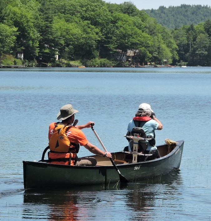 A paddler in the bow of a canoe is supported by a Creating Abilities seat with pads on the upper and lower back,and lateral pads on the sides.