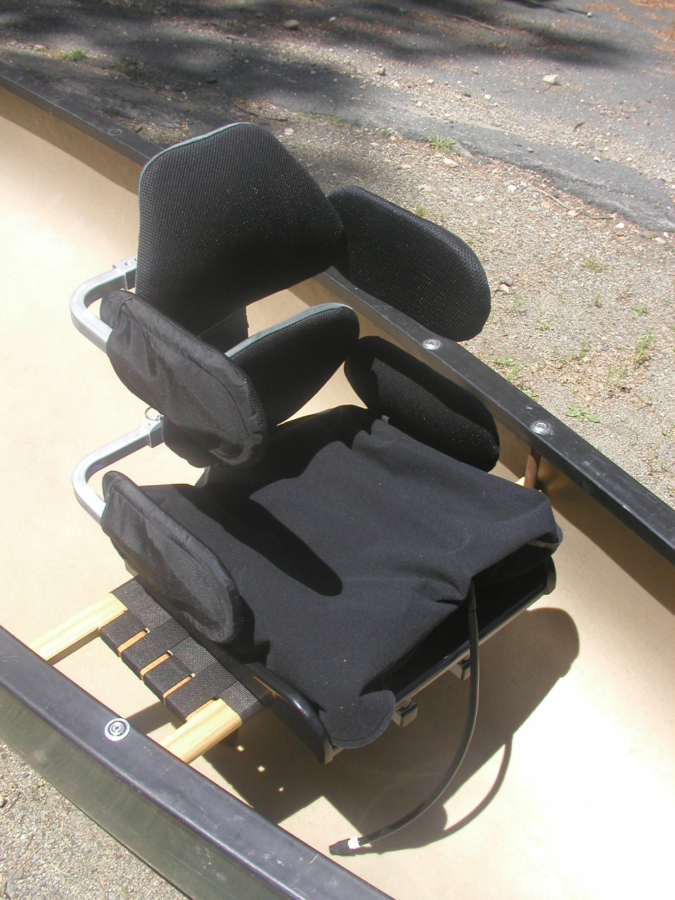 A seat mounted in a canoe. The seat has a trapezoidal pad at the lower back and another at upper back height. Two lateral support pads are located at the same height as each of the back pads, with four side pads total. There is a cushion in the bottom of the seat.