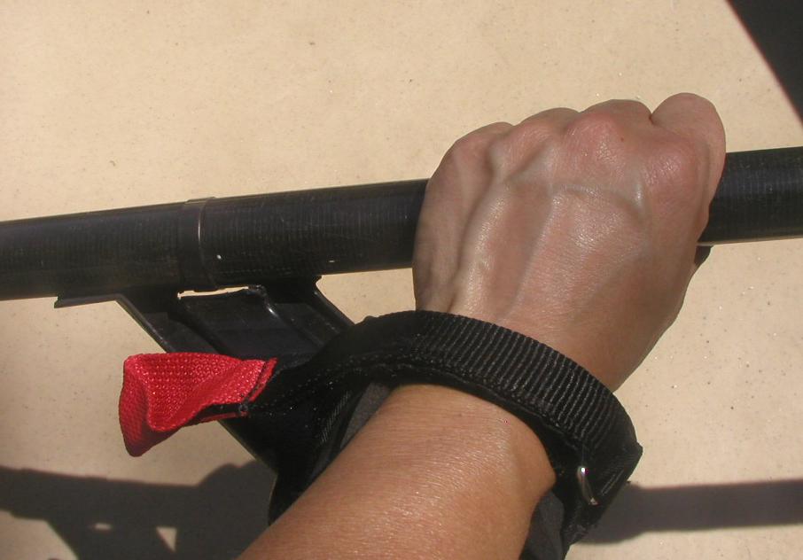 A hand grips a paddle. The hand has a cuff around the wrist that is attached to the paddle.