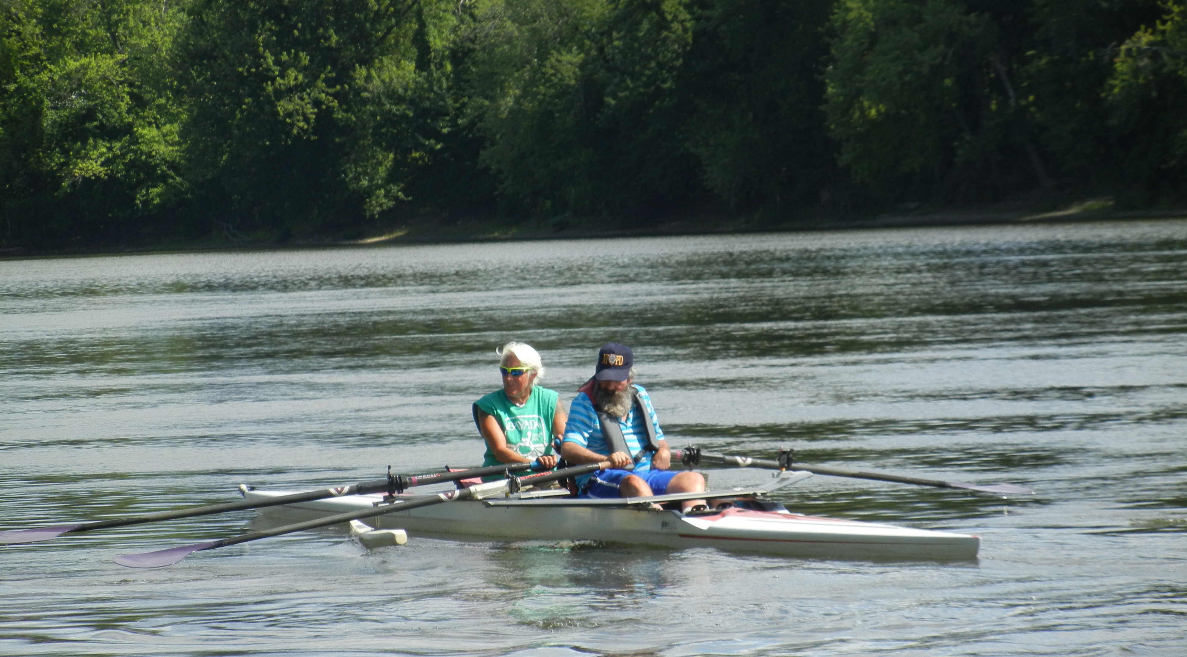 Two people are sculling in a double shell with outriggers on it.