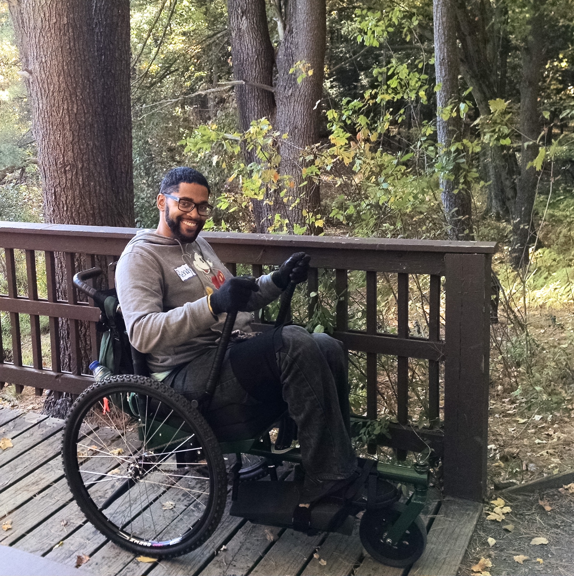 A hiker sitting in a GRIT Freedom chair on a deck next to a trail. The hiker is holding the levers.