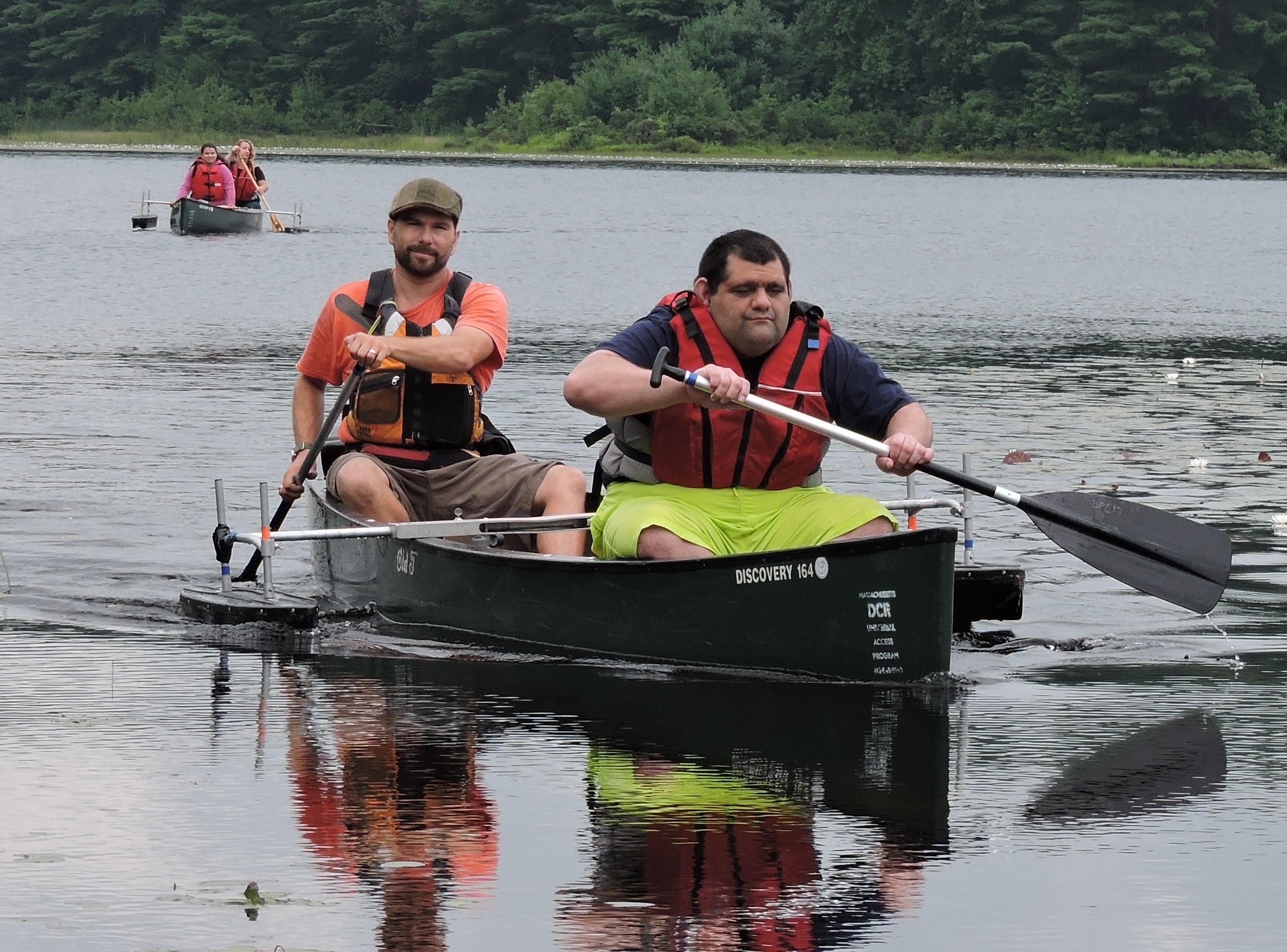 Two paddlers in a canoe with outriggers. Another canoe with outriggers is behind them.