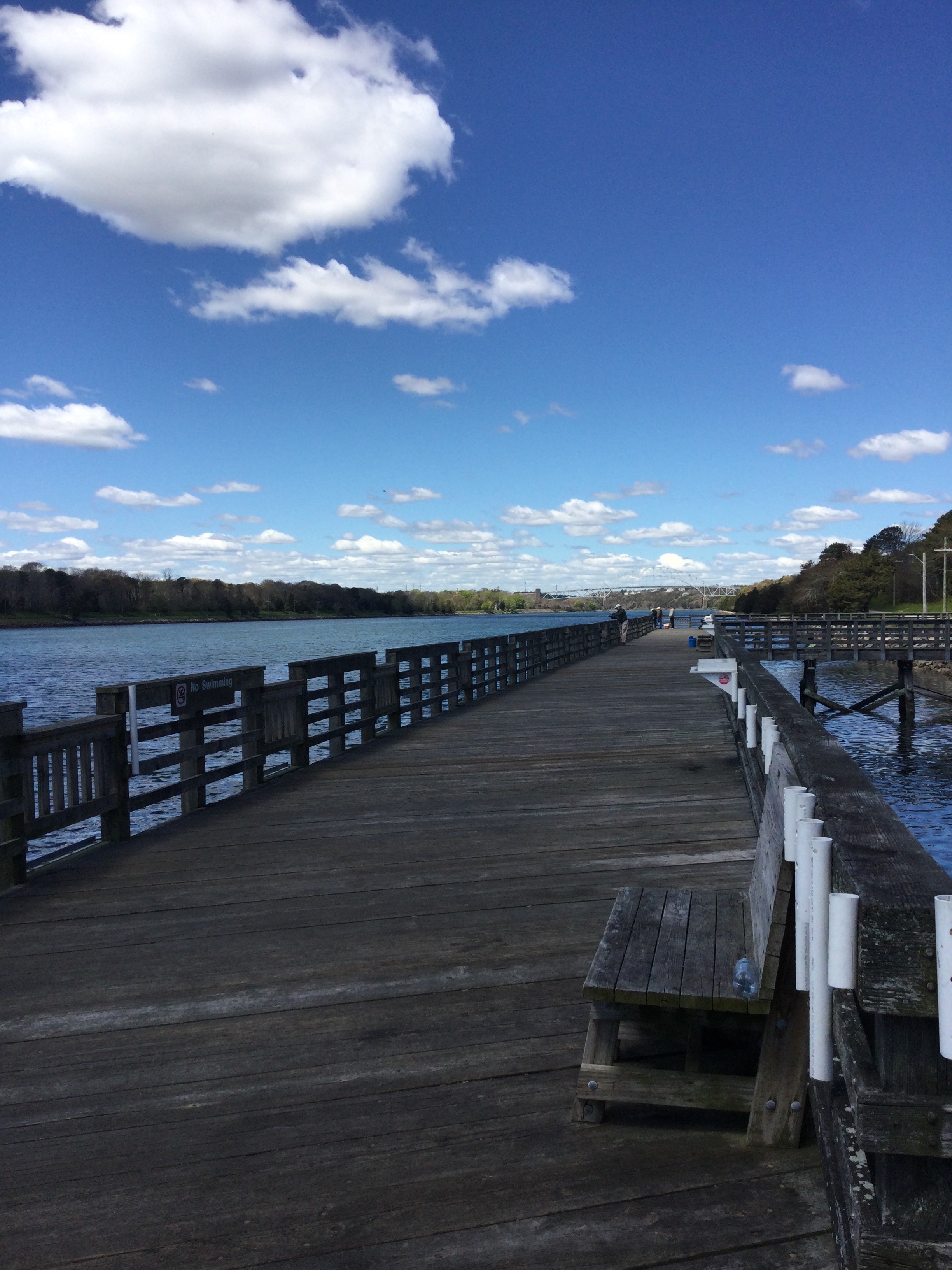 A long wooden pier with lowered areas along the railing. There are benches and rod holders.
