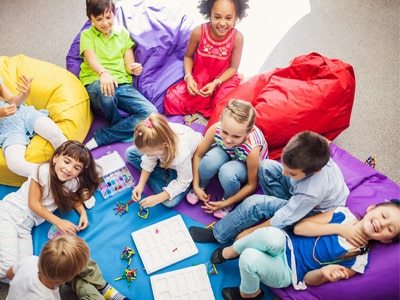 Children sitting together on bean bag chairs and coloring. 
