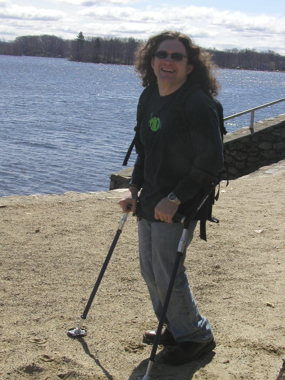A hiker using SideStix stands on a beach. The crutches have large tips with teeth.