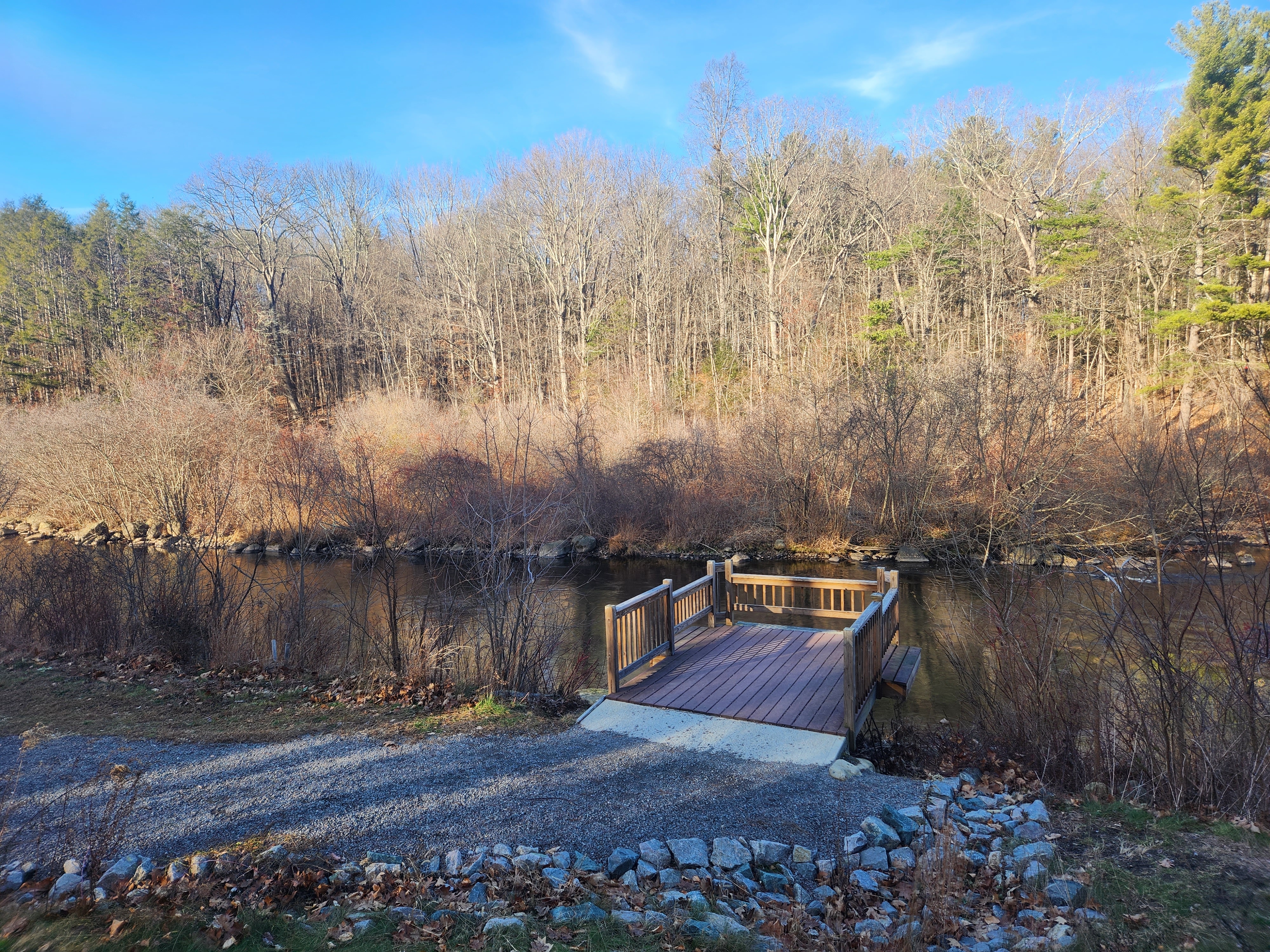 A stone dust path leads to a wooded platform with a railing overhanging a river.