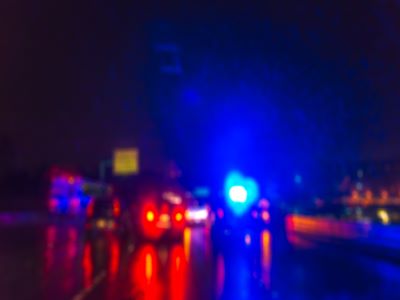 Rain blurs lights from emergency vehicles at a crash scene at night.