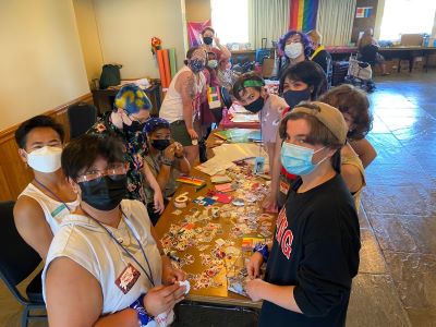 A group of masked LQBTQ youth commission members gather around a long table.