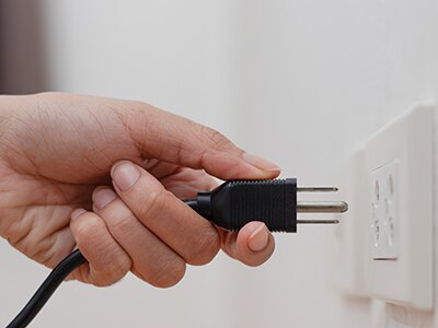 Hand plugging a cord into an electrical outlet. 