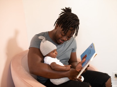 A Black adult reading to a Black infant