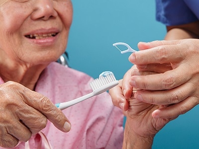 A senior woman is shown how to floss and brush her teeth.