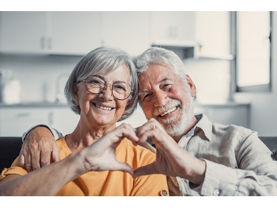 A photo of an elderly couple making a heart shape with their hands 