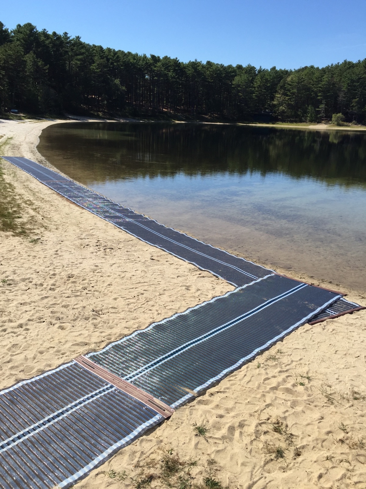 Beach mat runs up to the beach and along the water's edge at a pond surrounded by trees.