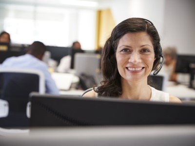 A smiling woman wearing a phone headset in an office