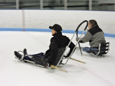 Two skaters on ice sleds in a skating rink.