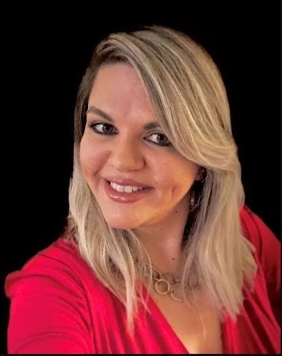 A Brazilian woman with blonde hair wearing a red blouse smiles in front of a black background.