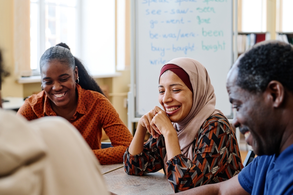 Three adults with different ethnicity backgrounds sitting at a table  in a meeting. They are all enjoying the meeting time together,