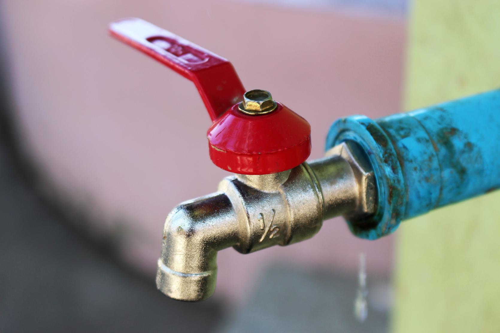 Outdoor water faucet with a red handle.