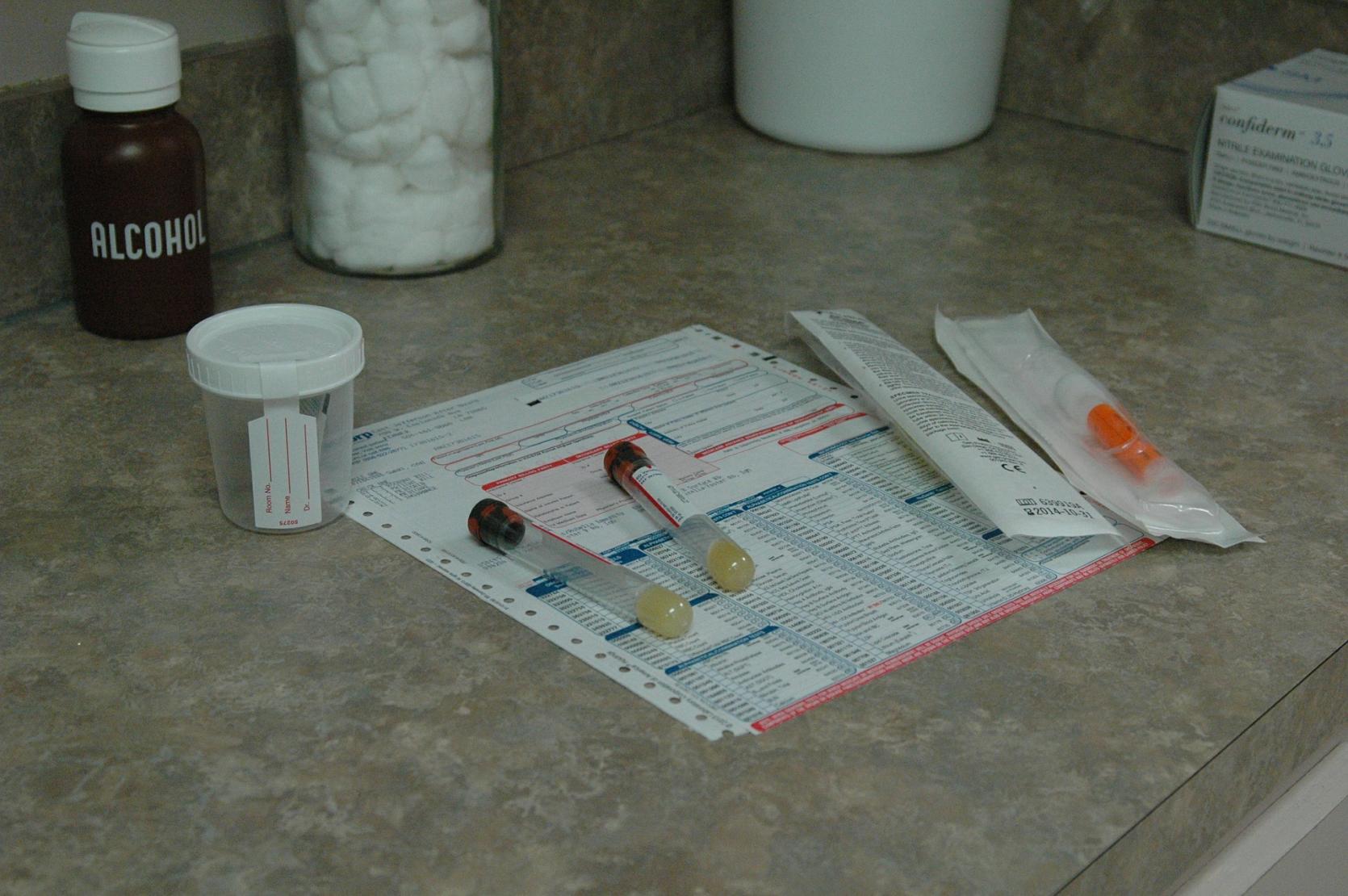 Plastic cup and vials for medical testing of urine and blood on a table with paperwork
