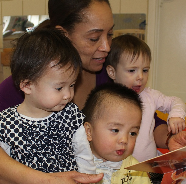 woman reading to three infants and toddlers