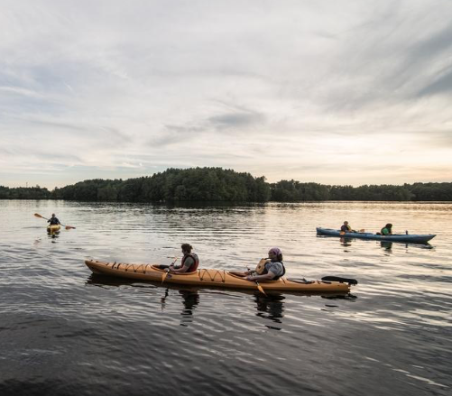 Three kayaks are out on the water as the sun is setting. Two of the kayaks are tandem kayaks with closed cockpits.