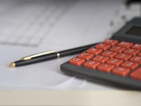 A business calculator and pen sitting on top of a printed spreadsheet. 