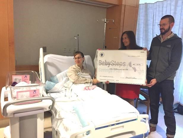 A photo of Treasurer Deborah Goldberg holding a big BabySteps check in a hospital room with two parents and a newborn baby.