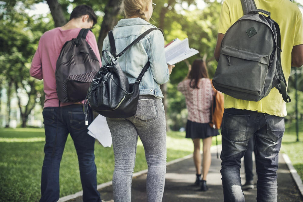 This is an image of the backs of four students walking on a campus with backpacks on as they walk to or from school