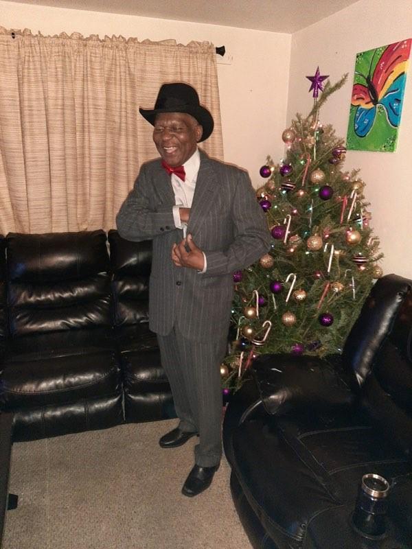 Photo of Inky standing in a suit and hat while smiling in front of holiday decorations