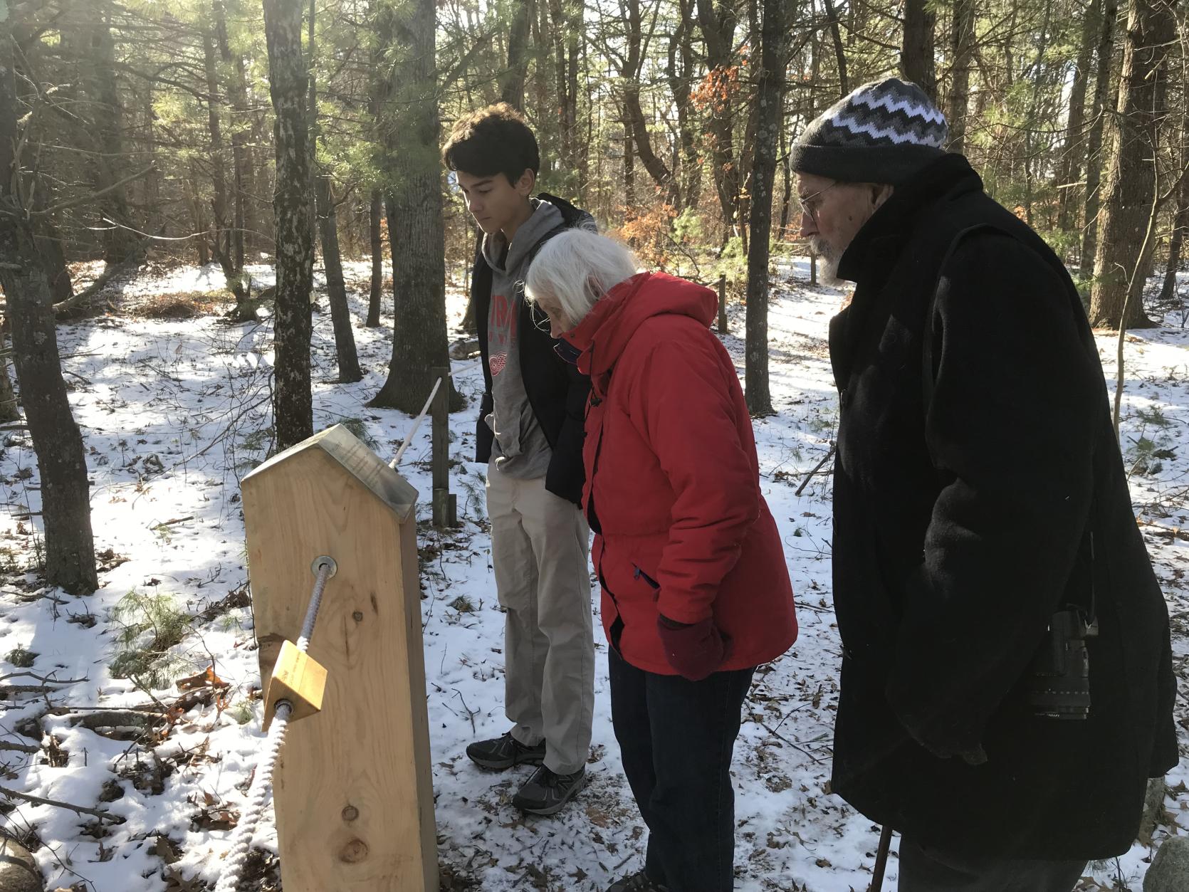 Andrew Hoadley on The Tupelo Trail for Blind Hikers with two other individuals reading one of the Braille markers
