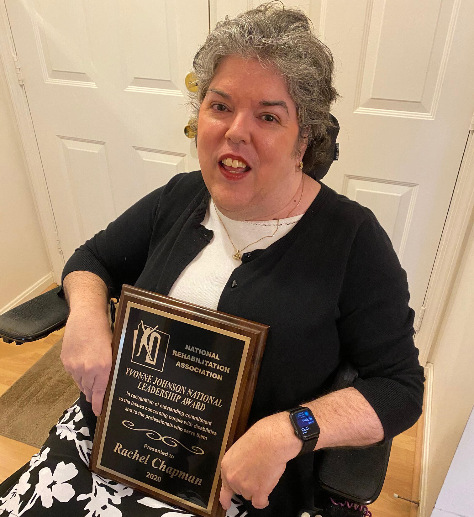 Woman in wheelchair sits holding black award plaque