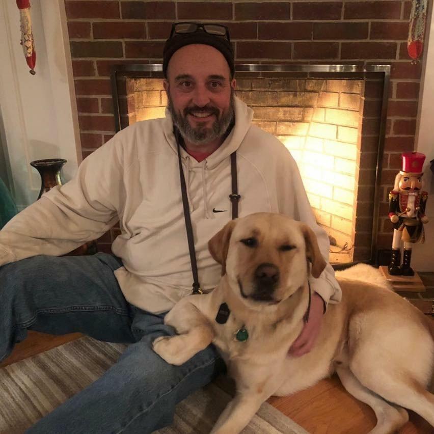 Steve Kapantais and Guide Dog Fritz sitting in front of fireplace