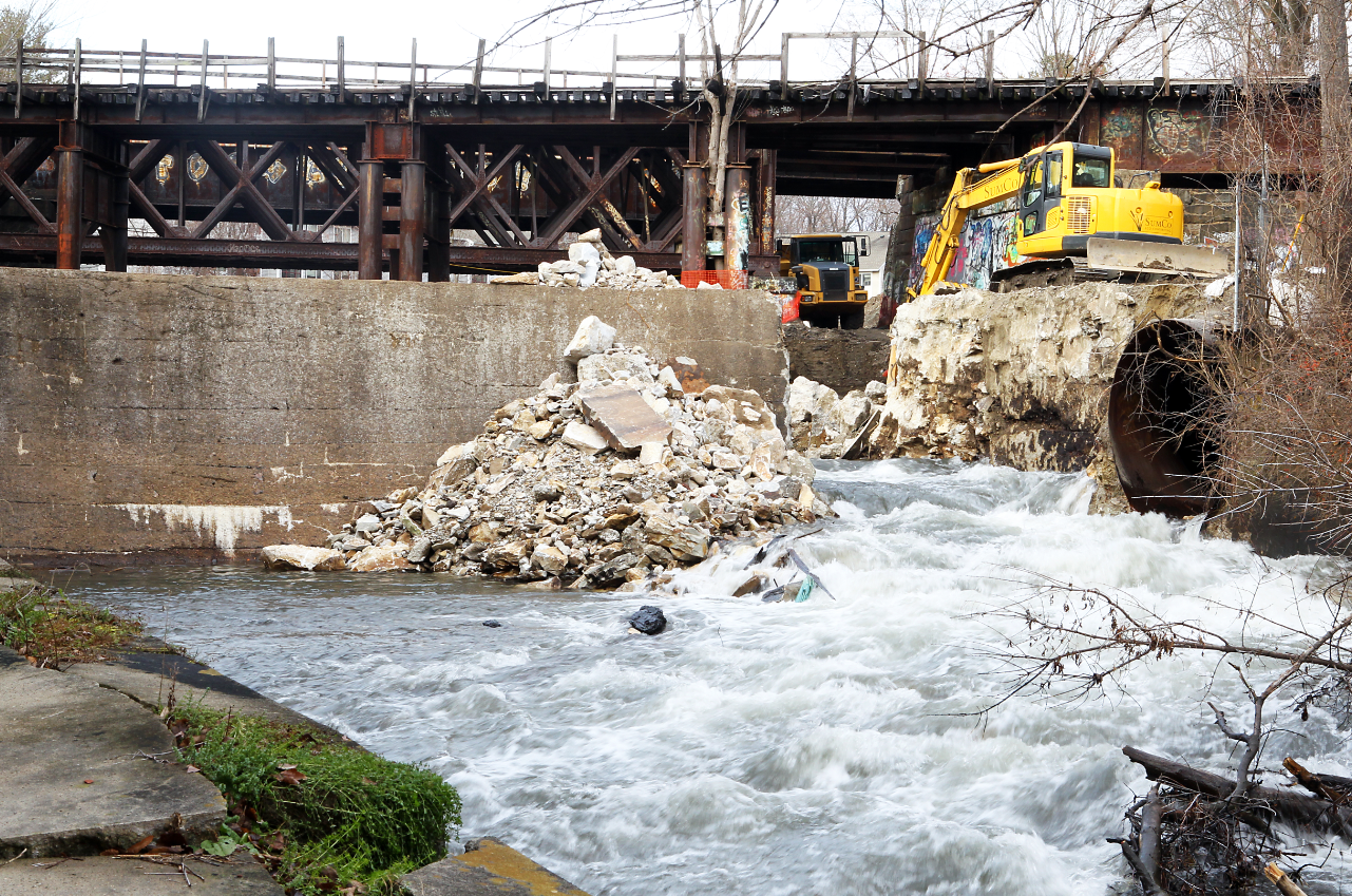 Construction equipment next to a partially removed concrete dam and a running river.