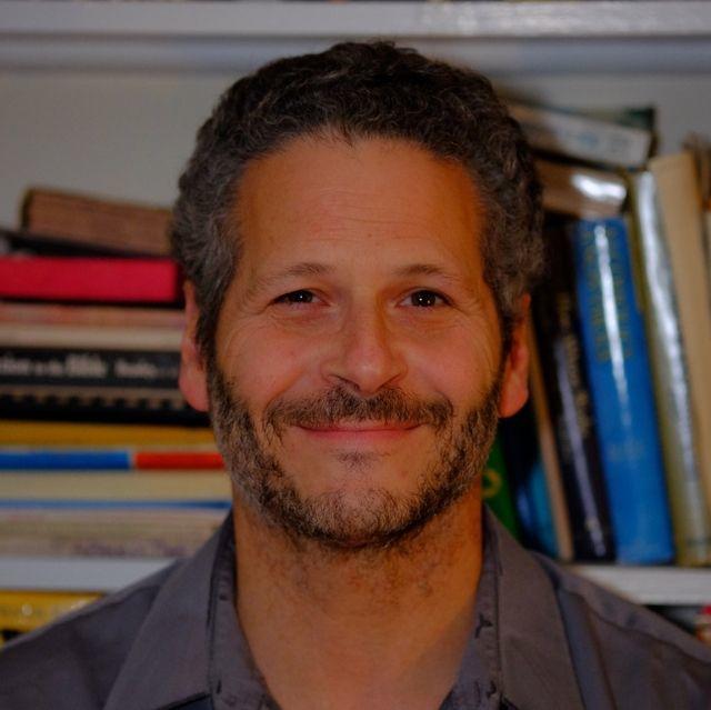 Headshot of Paul Hostovsky smiling in front of bookshelf