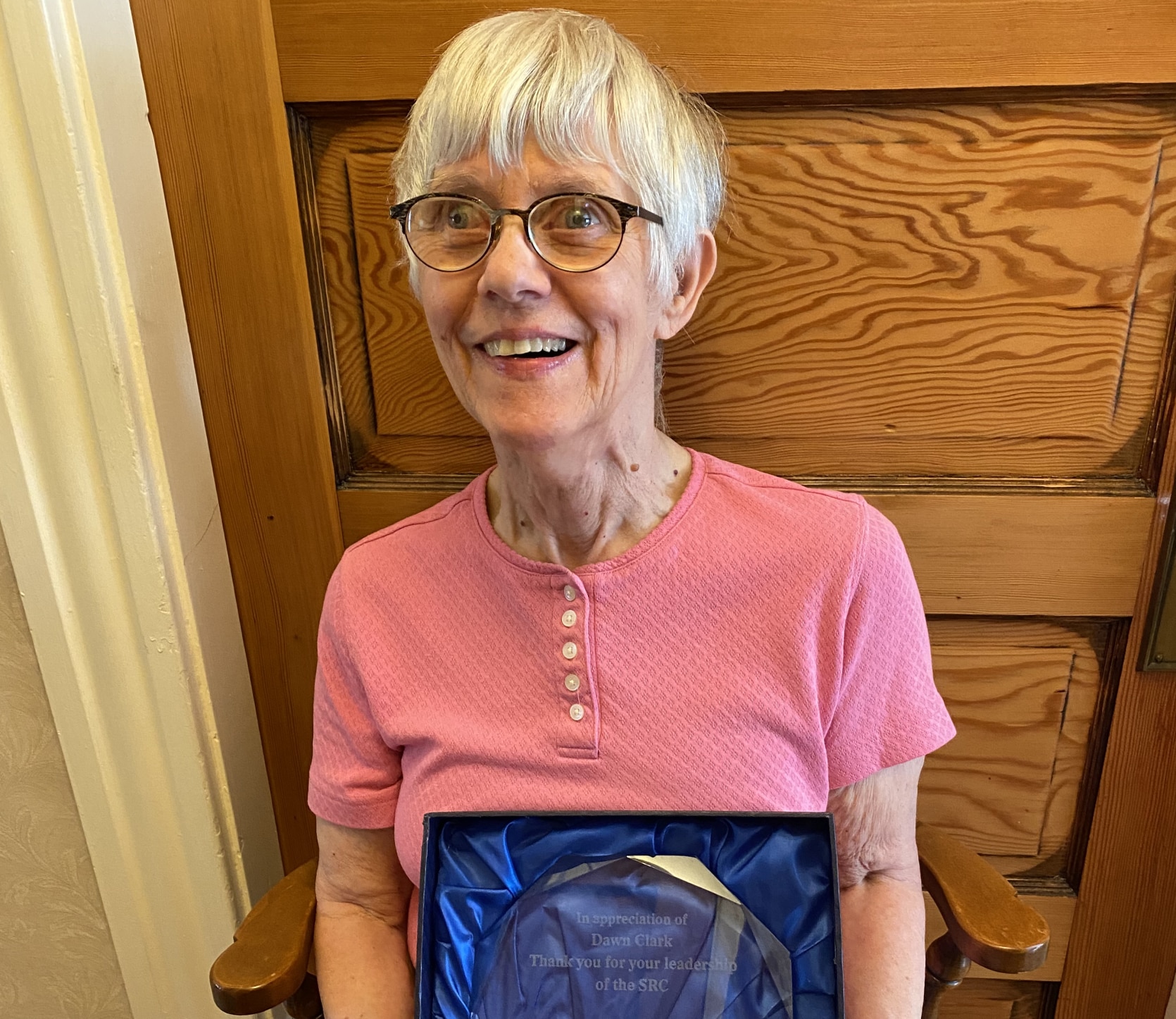 Dawn Clark holding an award from SRC. Silver hair, pink shirt.