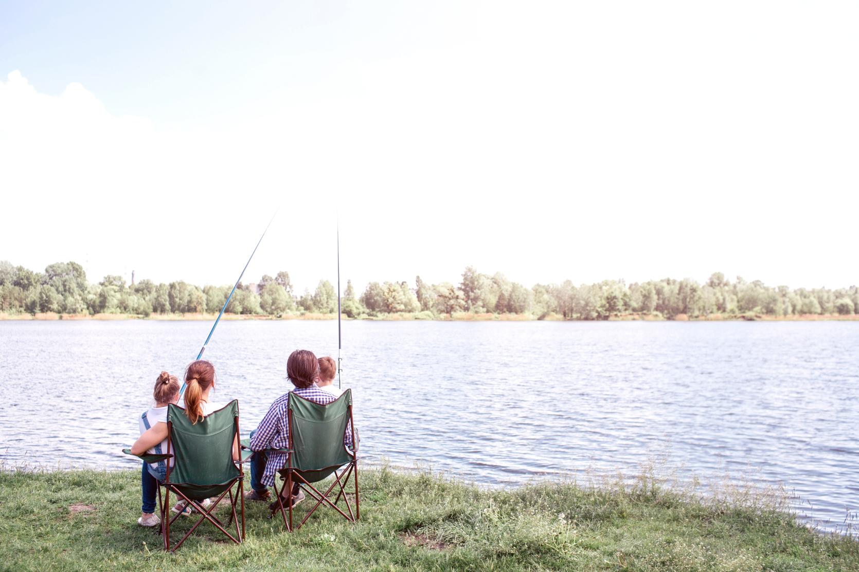 Parents and kids relax and fish from chairs on a bank by the water