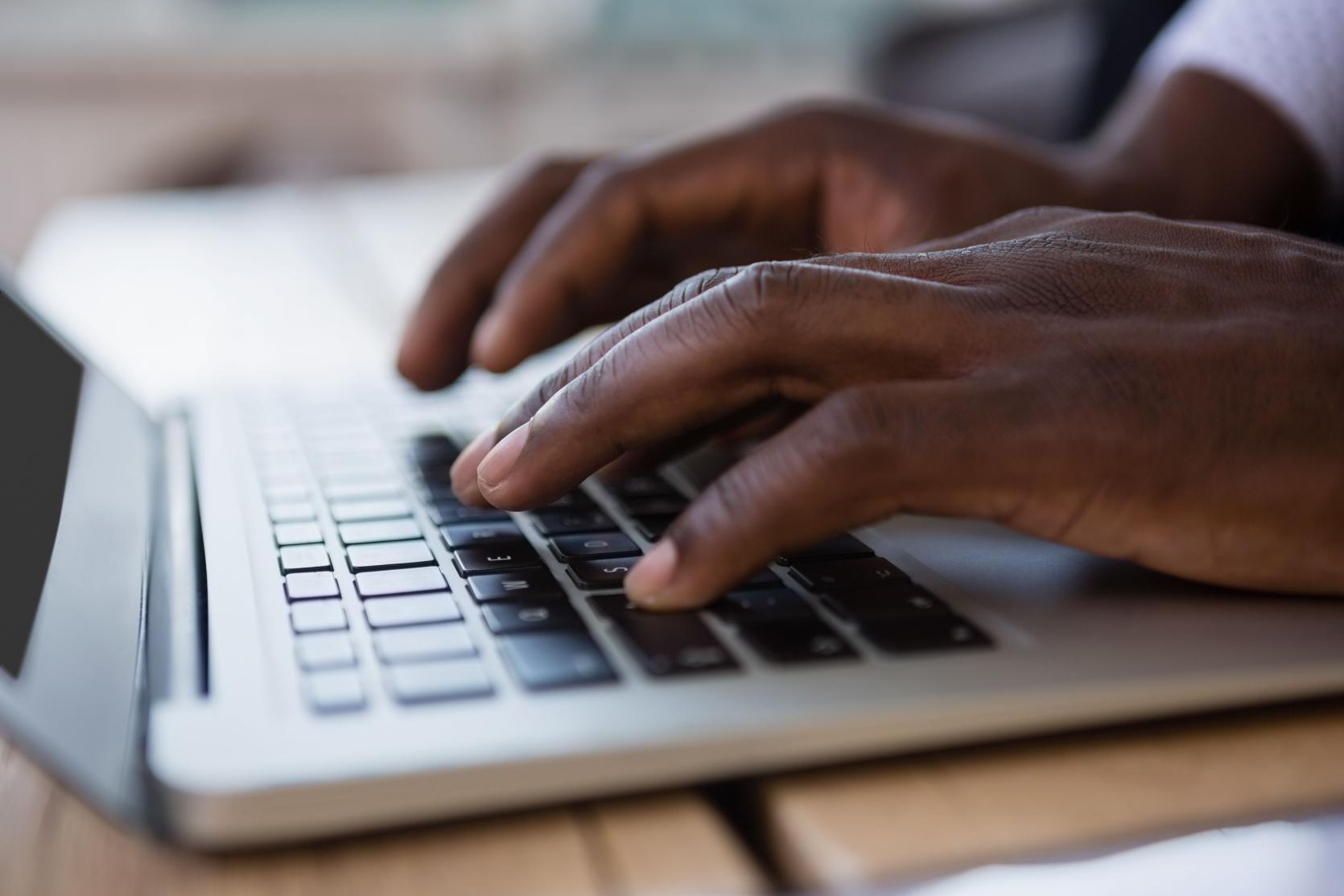 Close up of a Black man's hands typing on a laptop keyboard