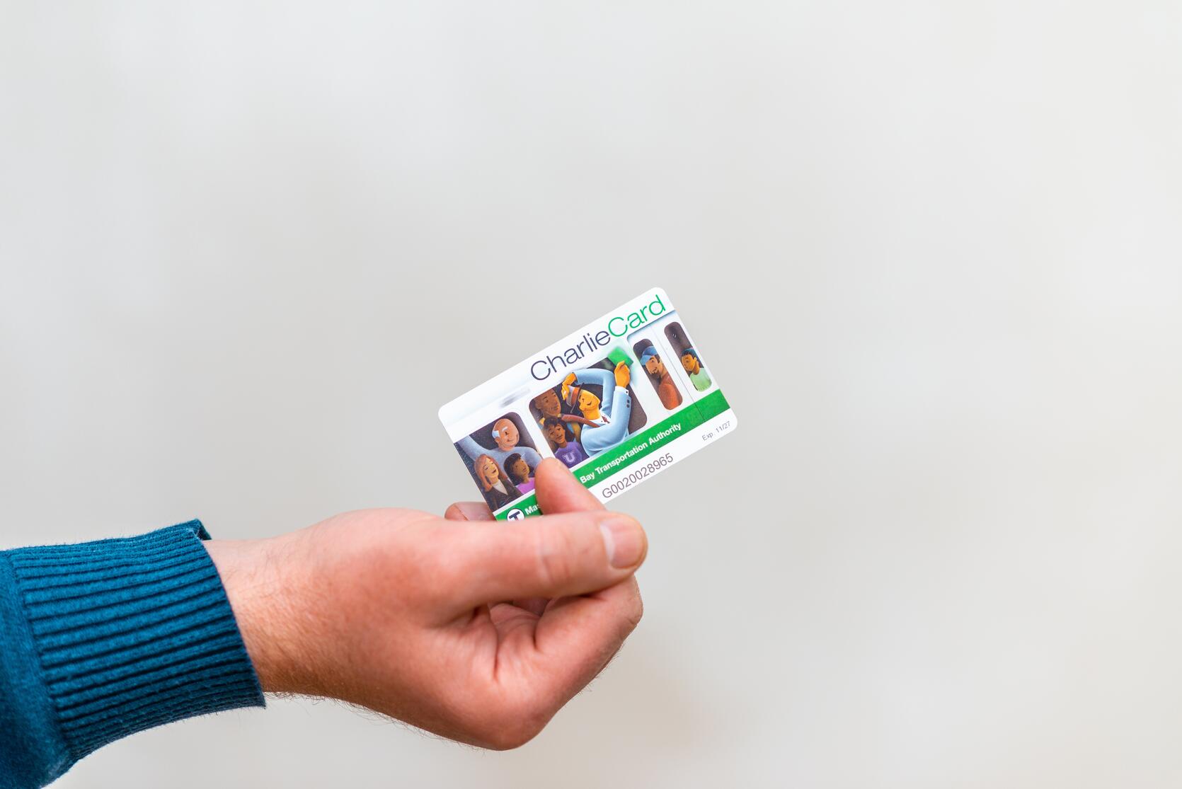 A close up photo of someone holding an MBTA CharlieCard against a white background.